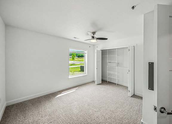 A room with a ceiling fan and a window showing a green lawn outside.