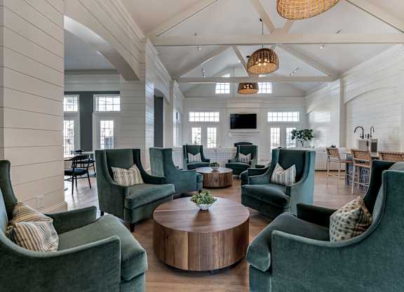 a large clubhouse lounge with green chairs and a table at Latitudes Apartments, Indianapolis, IN, 46237