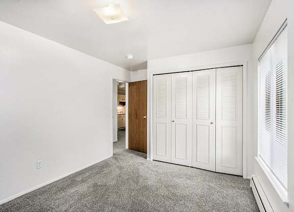 A bedroom with a large window and a grey carpet at Concord Place Apartments, Kalamazoo, MI