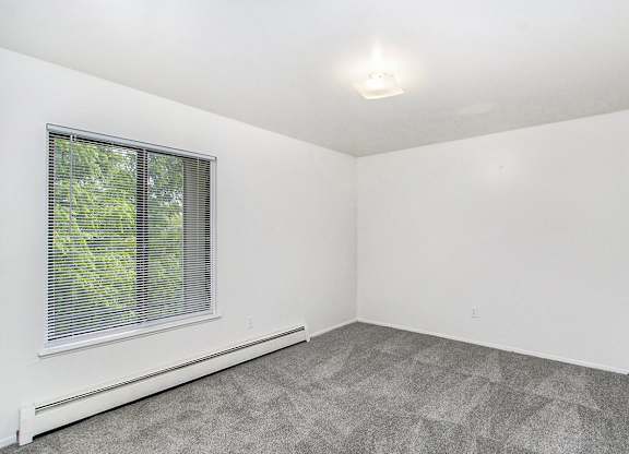 A bedroom with a window and carpeted floor at Concord Place Apartments, Kalamazoo, MI