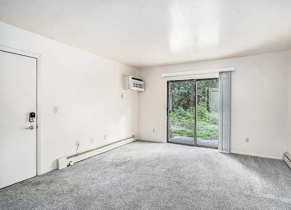 A living room with a carpet floor, a sliding glass door, and a white door at Concord Place Apartments, Kalamazoo, MI
