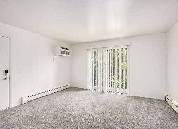 A living room with a sliding glass doors covered by blinds and a carpeted floor at Concord Place Apartments, Kalamazoo, MI