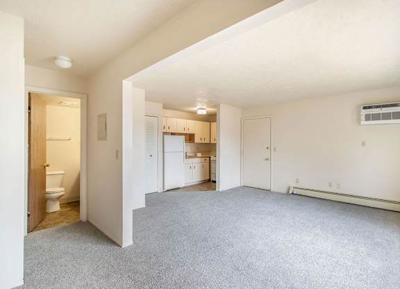 A spacious living room with a carpeted floor and a kitchen area in the background at Concord Place Apartments, Kalamazoo, MI, 49009