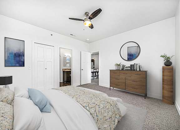 A bedroom with a bed, dresser, ceiling fan and ensuite at Copper Creek Apartment Homes, Maize, Kansas