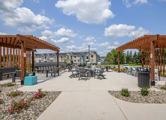 an outdoor pergola with tables and fire pit with seating at The Crossings Apartments, Michigan, 49508