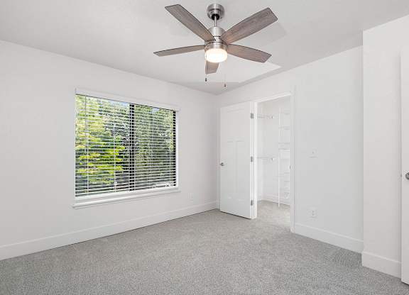 A bedroom with a ceiling fan and a window with blinds at The Crossings Apartments, Grand Rapids, Michigan