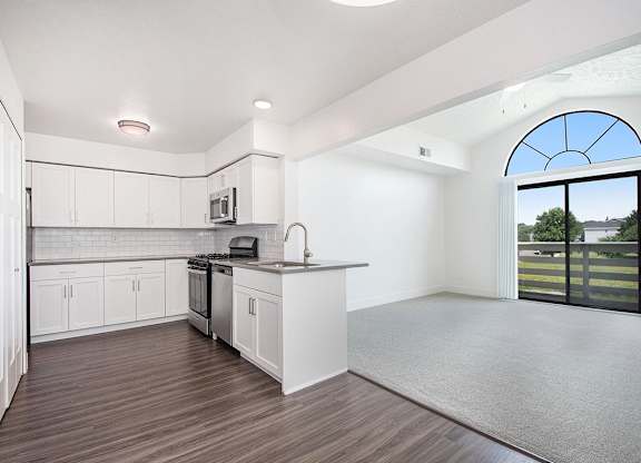 A kitchen with white cabinets and a living room with cathedral ceiling at The Crossings Apartments, Grand Rapids, MI, 49508