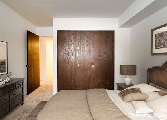 A bedroom with a large bed, a dresser, and a painting on the wall at Beacon Hill and Great Oaks Apartments, Rockford, Illinois