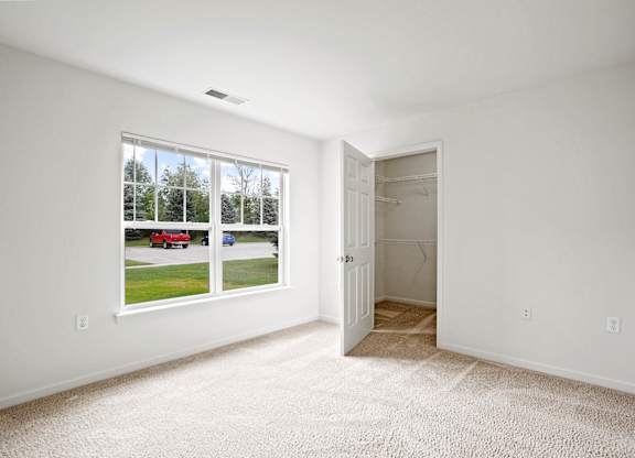 A room with a carpeted floor, a window with a view of a street, and a door leading to another room at Towne Lakes Apartments, Grand Chute