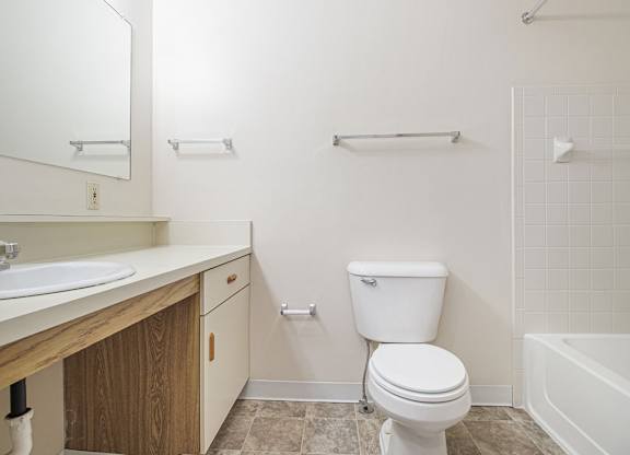 A white toilet sits in a bathroom next to a sink and a bathtub at Dupont Lakes Apartments, Fort Wayne