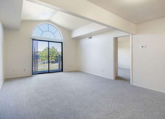A living room with a cathedral ceiling, large arched window and a carpeted floor at Dupont Lakes Apartments, Fort Wayne