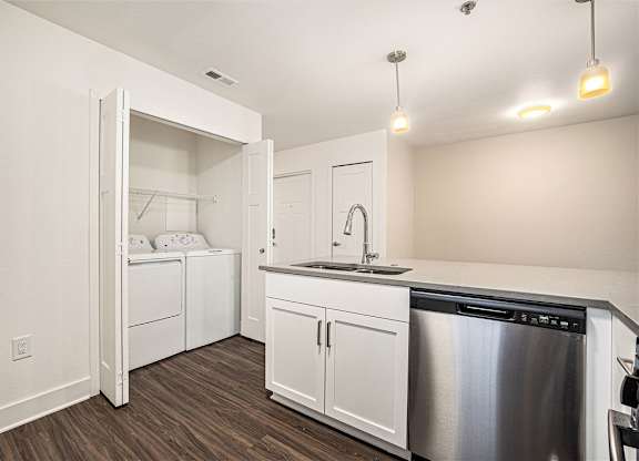 A modern kitchen with a stainless steel dishwasher and white cabinets and a full size washer and dryer at Eagle Ridge Apartment Homes, Traverse City, MI 49685