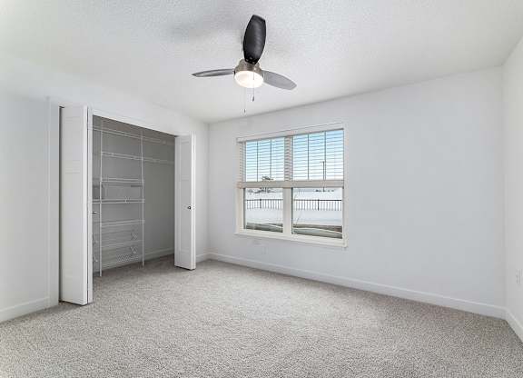 A spacious bedroom with a ceiling fan and large windows and a walk in closet with organizers at Eagle Ridge Apartment Homes, Traverse City, MI 49685
