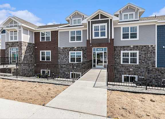 A multi-story residential apartment building with a sidewalk in front at Eagle Ridge Apartment Homes,  Michigan 49685