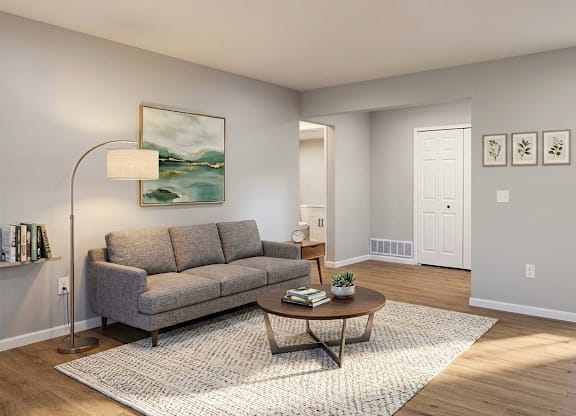 A living room with a grey couch, a round table, and a painting on the wall.