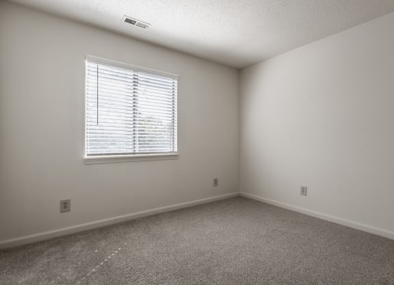 a bedroom with white walls and carpeted flooring and a window at Bavarian Village Apartments, Indianapolis, Indiana