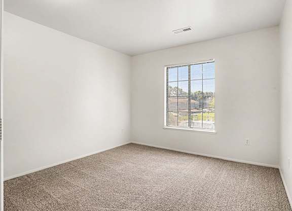 A bedroom with a carpeted floor and a large window at Emerald Park Apartments, Kalamazoo, Michigan
