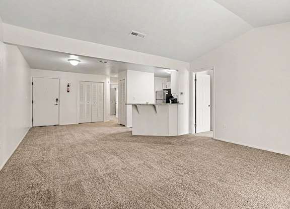 A large, empty living room with carpeted flooring and white walls at Emerald Park Apartments, Kalamazoo, Michigan