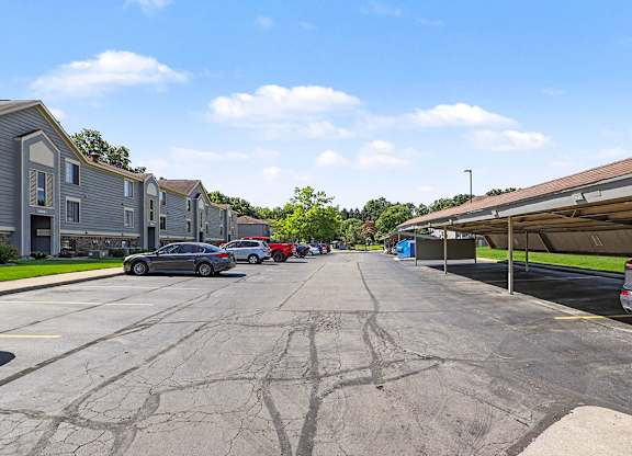 A parking lot with cars and carports with an apartment building in the background at Emerald Park Apartments in Kalamazoo, MI