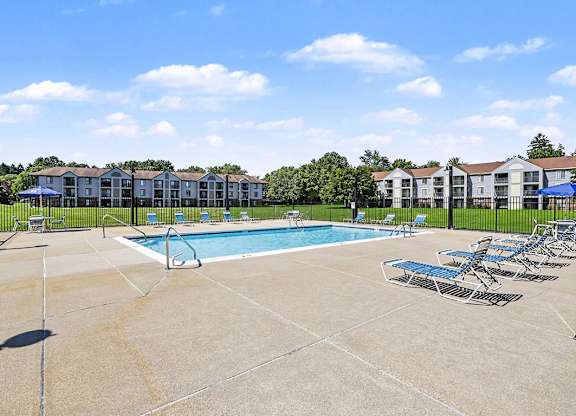 A swimming pool surrounded by chairs and apartment buildings in the background at Emerald Park Apartments in Kalamazoo, MI
