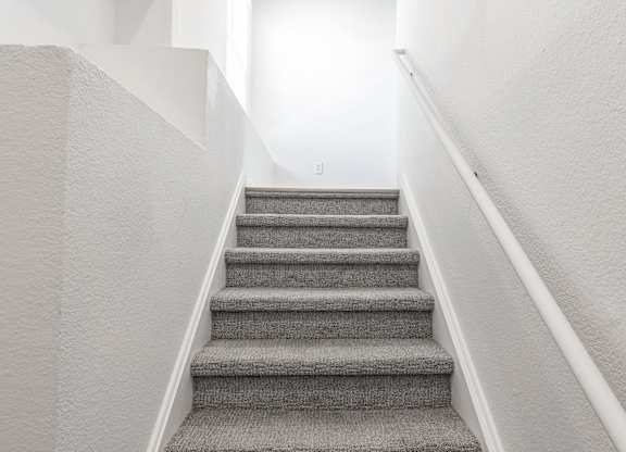 a staircase with grey carpeting and white walls and a white railing with a white at Latitudes Apartments, Indiana, 46237