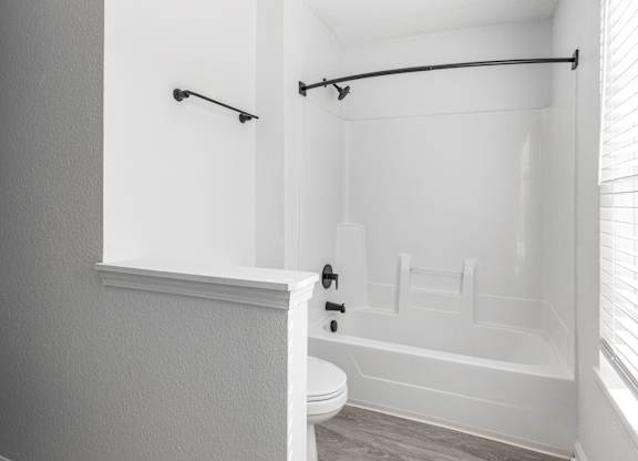 a white bathroom with a tub and a toilet and a window at Latitudes Apartments, Indianapolis, IN, 46237