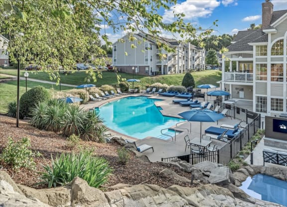 a resort style swimming pool with umbrellas in front of a building at The Vinings Apartments in Richmond, VA