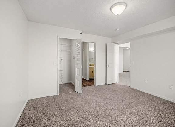 A white bedroom with a carpeted floor and an ensuite bathroom with a walk-in shower  at West Hampton Park Apartment Homes, Nebraska, 68022