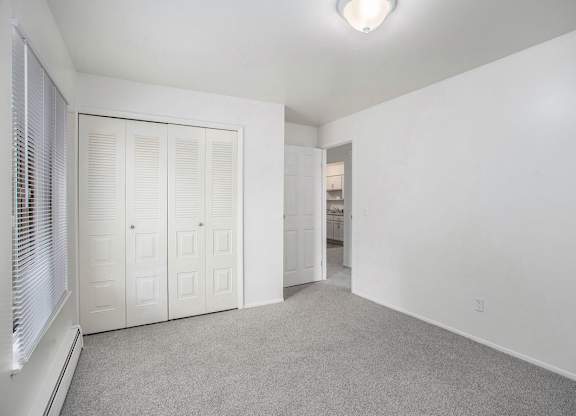 A bedroom with a grey carpet and a large white closet at Fairlane Apartments in Springfield, MI