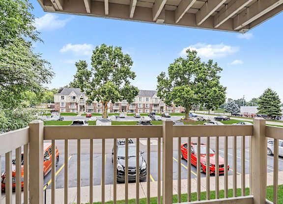 A view from a balcony overlooking a parking lot with cars and a building in the background.