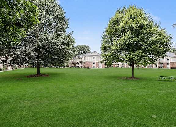 A grassy field with trees and a bench in front of a building at Fairlane Apartments, Springfield, MI 49037