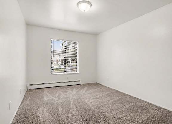 Vacant carpeted bedroom with window and heater at Fairlane Apartments, Springfield, MI 49037