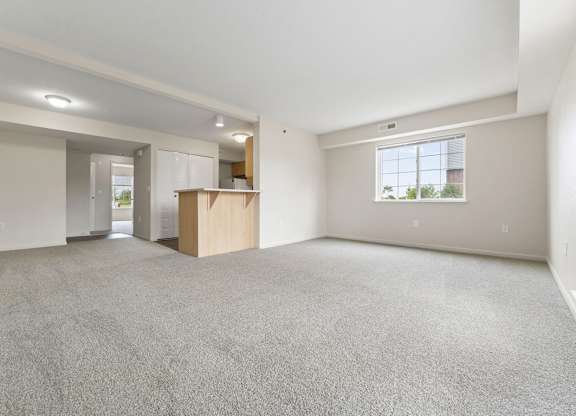 A large, empty living room with a carpeted floor and a window at Fieldstream Apartment Homes in IA 50023