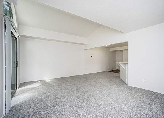 A large, empty living room with white walls and a grey carpet at Foxwood and The Hermitage in Portage, MI