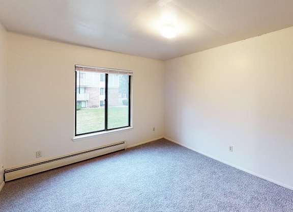 A large bedroom with a window and a carpeted floor at Glen Oaks Apartments, Michigan, 49442
