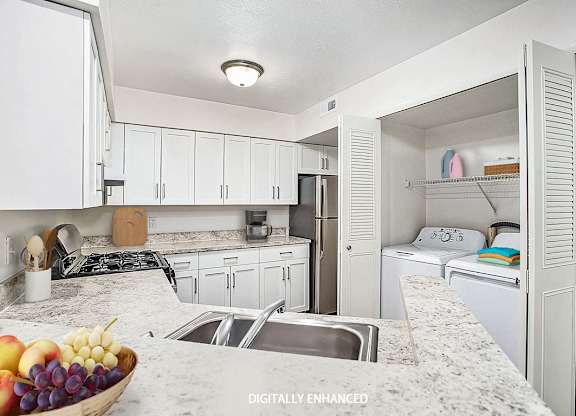 A kitchen with white shaker style cabinets and a washer and dryer at Glenn Valley Apartments in Battle Creek, MI