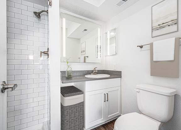 A white toilet is in a bathroom with a white tiled shower at Green Ridge Apartments, Grand Rapids, MI