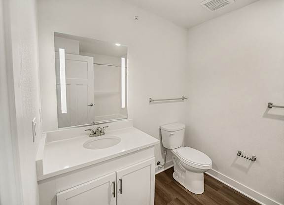 A white bathroom with a toilet, sink, and mirror at The Grove Apartment Homes in Lincoln, NE