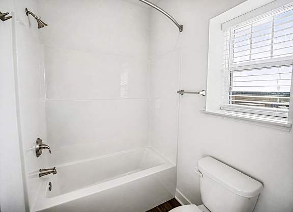 A white bathroom with a toilet and a bathtub at The Grove Apartment Homes in Lincoln, NE