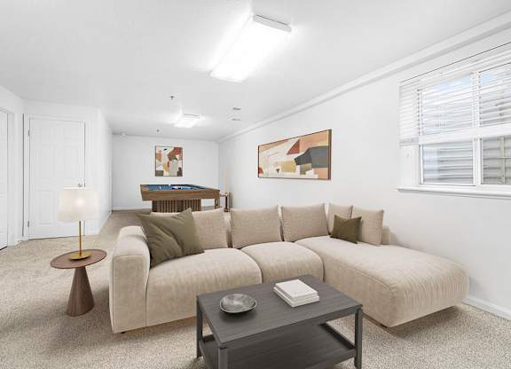 A basement recreation room with a beige couch, a coffee table, and a lamp at Gull Prairie/Gull Run Apartments and Townhomes, Michigan