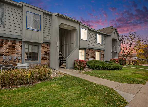 A grey building with a brick wall and landscaping in front at Hampton Lakes Apartments, Walker, 49534