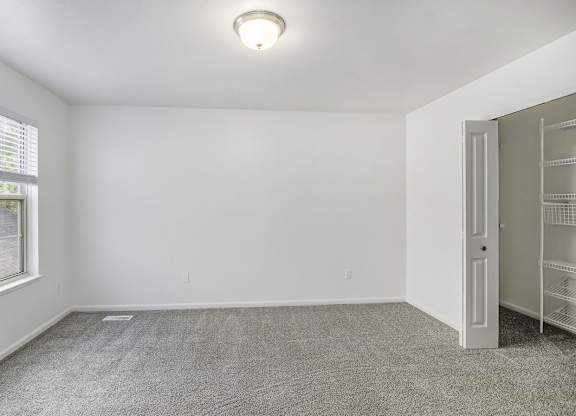 A bedroom with a grey carpet and a walk-in closet at Foxwood and The Hermitage, Portage, MI, 49024