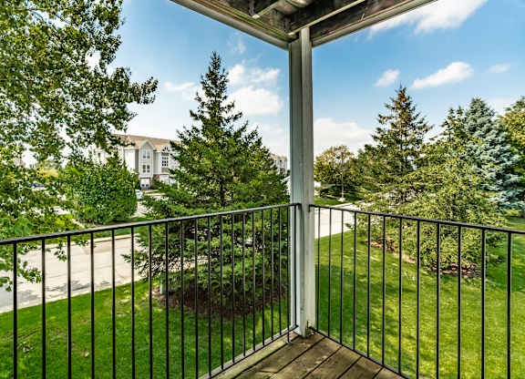 A balcony with a black railing and a view of a tree and a building in the background