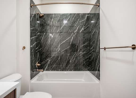 A bathroom with a marble wall and a white bathtub.