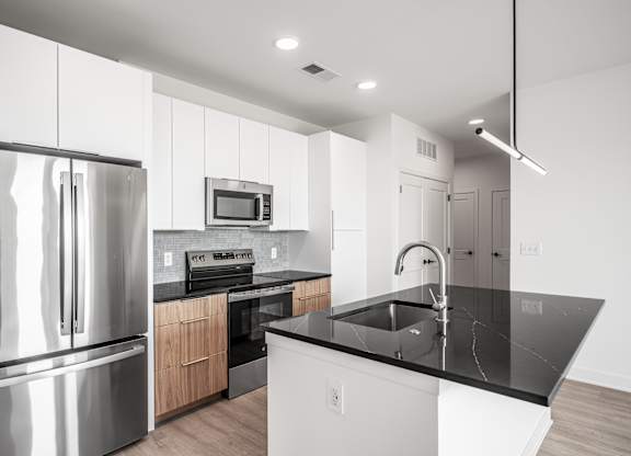 A modern kitchen with a stainless steel refrigerator and black countertops.
