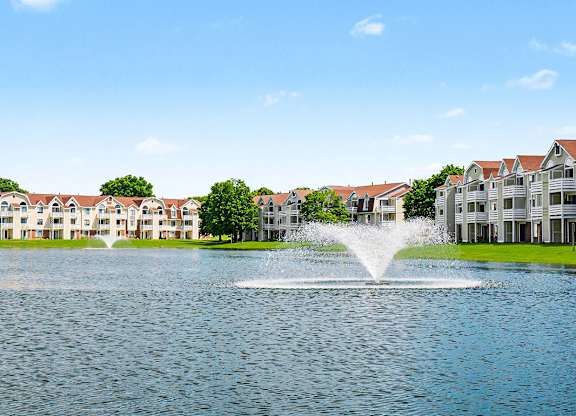 A fountain in the middle of a pond in front of apartment buildings at Indian Lakes Apartments, Mishawaka, Indiana