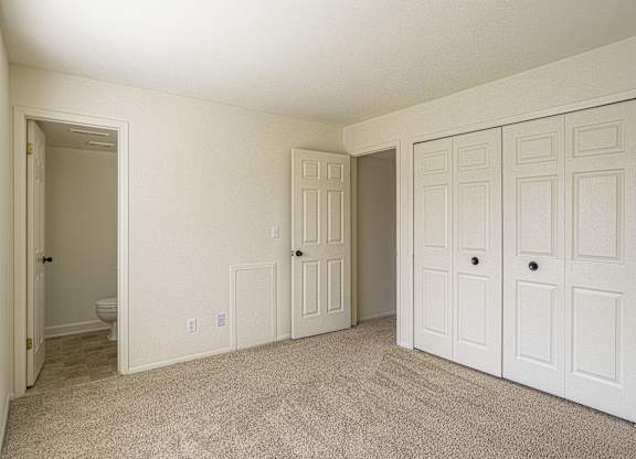 A room with white walls and carpeted floor with two doors.