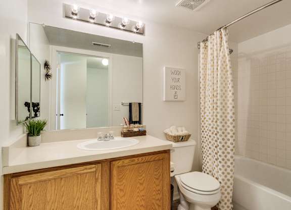 A bathroom with a mirror, sink, toilet and a shower curtain  at Northport Apartments, Macomb, MI, 48044