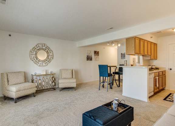 A living room with a white couch, two chairs, a coffee table, and a kitchen area in the background  at Northport Apartments, Macomb, MI, 48044