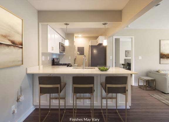 a kitchen with white cabinets and a large island with four stools at Hillside Apartments, Wixom, MI, 48393
